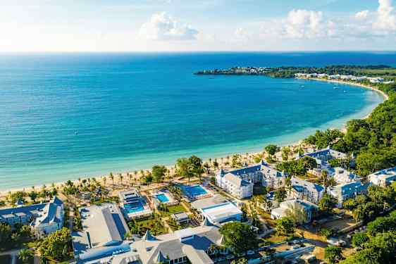 Kuva rannikkoalueesta turkoosilla vedellä, valkoisella hiekkarannalla ja lähellä sijaitsevista hotellirakennuksista. (Tekoälyn luoma teksti)