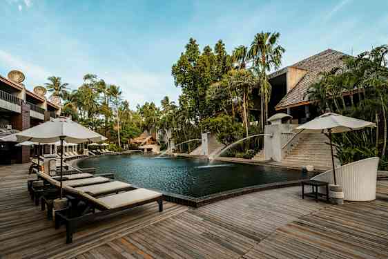 Ulkouima-allas, jonka ympärillä on puuterassi ja aurinkotuoleja varjoineen. Taustalla näkyy vehreää kasvillisuutta ja rakennuksia, joissa on puu- ja kivirakenteita. (Tekoälyn luoma teksti)