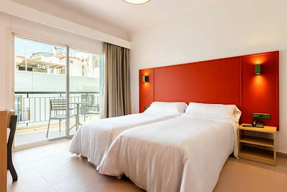 Huone, jossa on kaksi valkoisilla vuodevaatteilla varustettua yhden hengen vuodetta, punainen sängynpääty ja parveke ulkopuolella. (Tekoälyn luoma teksti)