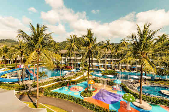 Kuva hotellialueesta, jossa on uima-altaita, vesiliukumäki ja värikkäitä leikkialueita palmujen ympäröimänä. (Tekoälyn luoma teksti)