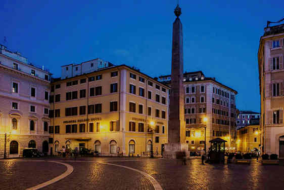 Aukio, jota ympäröivät rakennukset ja jonka keskellä on obeliski, valaistu yöllä. (Tekoälyn luoma teksti)
