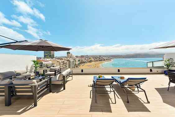 Katoterassi, jossa on huonekaluja, aurinkovarjo ja näkymä rannalle ja merelle. (Tekoälyn luoma teksti)
