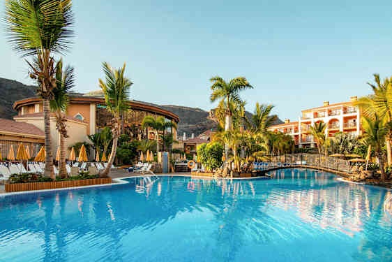 Kuva hotellialueesta, jossa on uima-allas, palmuja ja rakennuksia ympärillä. (Tekoälyn luoma teksti)