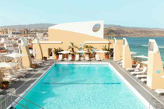 Kattoterassi, jolla uima-allas, aurinkotuoleja ja aurinkovarjoja näkymällä kaupunkiin ja merelle. (Tekoälyn luoma teksti)