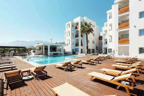 Ulkouima-allasalue, jossa aurinkotuoleja, moderni rakennus ja sininen taivas. (Tekoälyn luoma teksti)