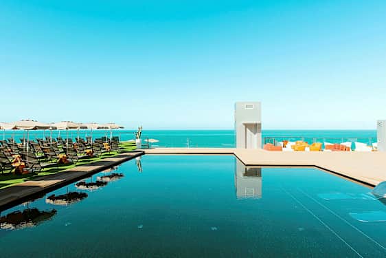 Uima-allas meren äärellä, jossa aurinkotuoleja ja aurinkovarjoja. (Tekoälyn luoma teksti)