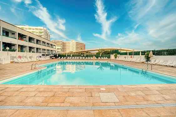 Ulkoilma-allas hotellin luona, jossa aurinkotuoleja ja sininen taivas. (Tekoälyn luoma teksti)