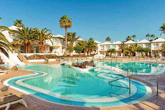 Hotellin uima-allas, jonka ympärillä on palmuja, aurinkotuoleja ja valkoisia rakennuksia. (Tekoälyn luoma teksti)