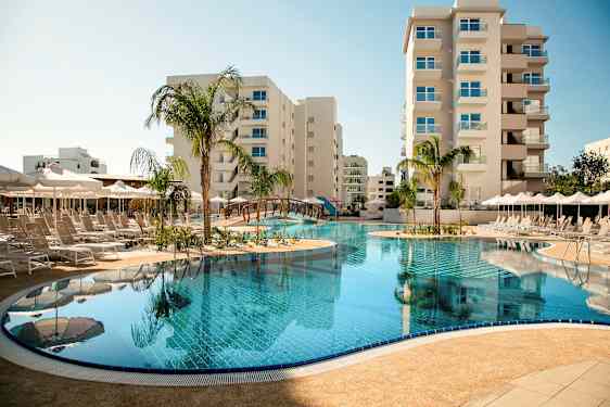 Ulkouima-allas, jota ympäröivät aurinkotuolit ja aurinkovarjot, taustalla korkeat rakennukset. (Tekoälyn luoma teksti)