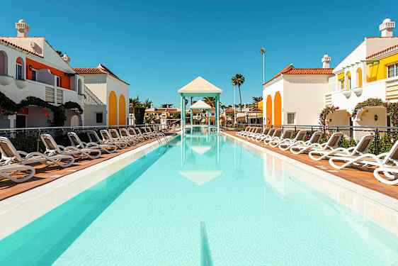 Ulkouima-allas, jonka ympärillä on aurinkotuoleja ja värikkäitä rakennuksia kirkasta taivasta vasten. (Tekoälyn luoma teksti)