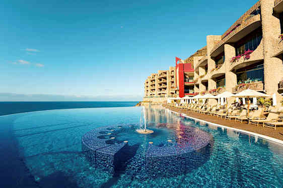 Infinity-allas rannalla, taustalla aurinkotuoleja ja hotellirakennuksia. (Tekoälyn luoma teksti)