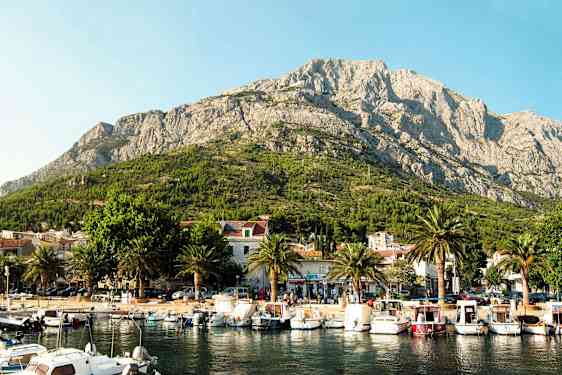 Satama veneineen pienen kaupungin edessä, taustalla vuoret. (Tekoälyn luoma teksti)