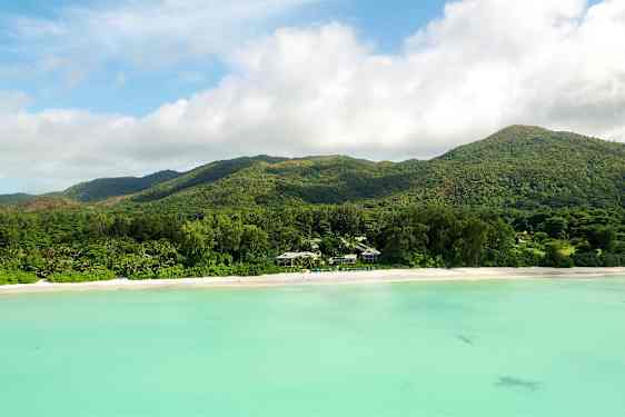 Ranta, jossa on valkoista hiekkaa, metsän peittämä vuorijono ja turkoosia vettä. (Tekoälyn luoma teksti)