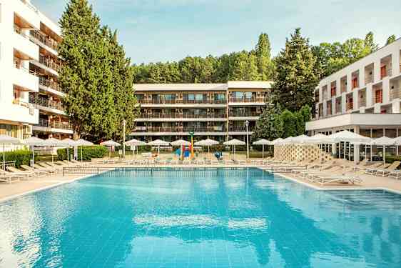 Ulkouima-allas, jonka ympärillä aurinkotuoleja ja varjoja, ympäröitynä modernilla rakennuksilla ja vehreydellä. (Tekoälyn luoma teksti)