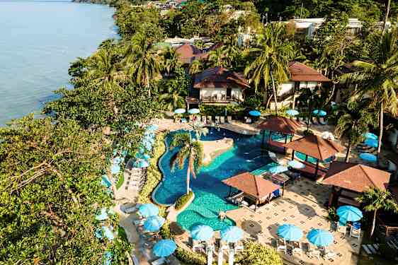 Lomakeskus, jossa on uima-allas, palmuja ja aurinkovarjoja meren äärellä. (Tekoälyn luoma teksti)