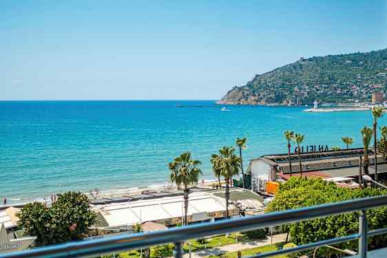 Näkymä merelle ja rannalle, jossa on rakennuksia etualalla. Taustalla näkyy niemimaa, jolla on asutusta. (Tekoälyn luoma teksti)