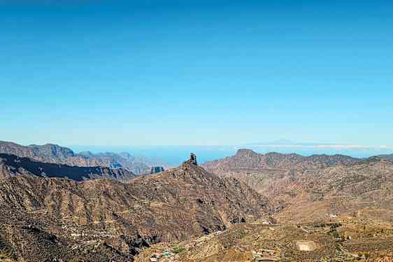 Maisema vuorilla ja erottuva kalliomuodostuma sinisen taivaan alla. (Tekoälyn luoma teksti)