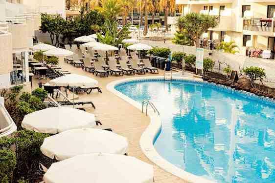 Uima-allasalue aurinkotuoleilla ja varjoilla hotellin vieressä. (Tekoälyn luoma teksti)