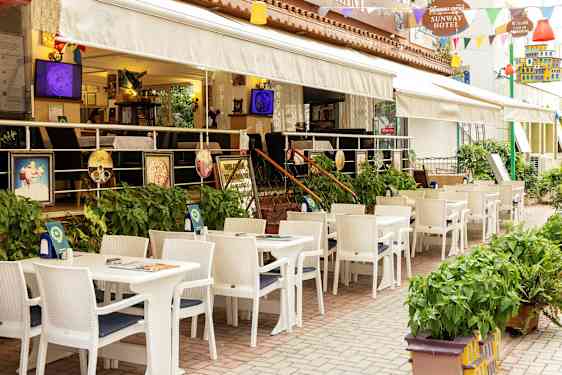 Ravintola ulkoterassilla, valkoiset pöydät ja tuolit hotellin vieressä. (Tekoälyn luoma teksti)