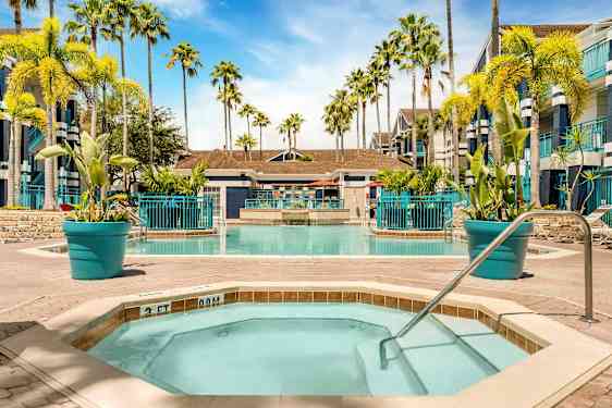 Kuva uima-altaasta, jota ympäröivät aurinkotuolit ja palmut. Etualalla on pienempi poreallas kaiteineen. (Tekoälyn luoma teksti)