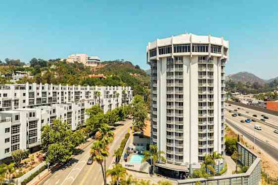 Moderni, korkea rakennus, jota ympäröivät tiet, vehreys ja muut rakennukset. (Tekoälyn luoma teksti)