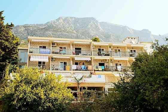 Rakennus, jossa on parvekkeita ja roikkuvia pyyhkeitä, ympärillä vehreyttä ja vuoret taustalla. (Tekoälyn luoma teksti)