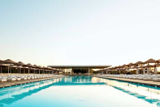 Suuri ja pitkä uima-allas, jonka molemmin puolin on aurinkovarjoja ja aurinkotuoleja. (Tekoälyn luoma teksti)