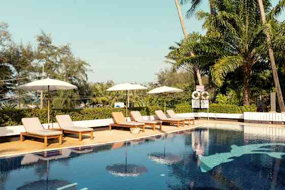 Ulkouima-allas, jossa on aurinkotuoleja ja sateenvarjoja. Taustalla trooppisia puita. (Tekoälyn luoma teksti)