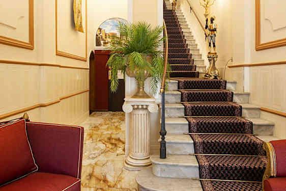 Tyylikäs eteinen, jossa punaisia huonekaluja ja kuvioidulla matolla varustettu portaikko. (Tekoälyn luoma teksti)