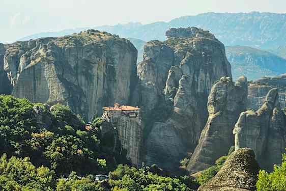 Luostari sijaitsee kalliomuodostelman päällä, ympärillään vihreitä metsiä ja vuoria. (Tekoälyn luoma teksti)