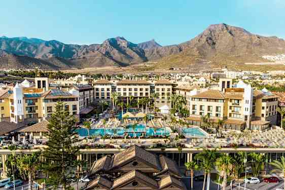 Hotellirakennukset, uima-allasalue ja vuoret taustalla. (Tekoälyn luoma teksti)