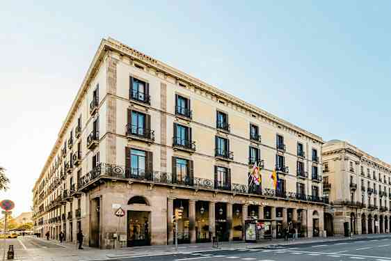 Kadun kulma, jossa on klassista tyyliä edustava rakennus, jossa on useita kerroksia, kaaria ja koristeellisia parvekkeita. (Tekoälyn luoma teksti)