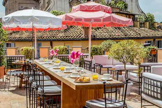 Terassi, jossa istuinryhmiä, aamiaistarjoilua ja aurinkovarjoja aurinkoisessa säässä. (Tekoälyn luoma teksti)