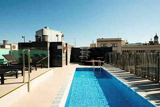 Ulkouima-allas kattoterassilla, jota ympäröivät aurinkotuolit ja rakennuksia taustalla. (Tekoälyn luoma teksti)