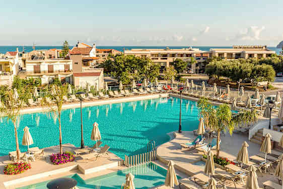 Ulkouima-allas, jota ympäröivät aurinkotuolit ja aurinkovarjot, taustalla rakennuksia ja meri. (Tekoälyn luoma teksti)