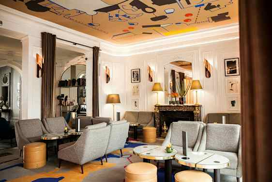 Tyylikäs olohuone, jossa harmaita sohvia ja nojatuoleja, marmorisia pöytiä, koristeellinen takka ja taideteoksia seinällä. (Tekoälyn luoma teksti)