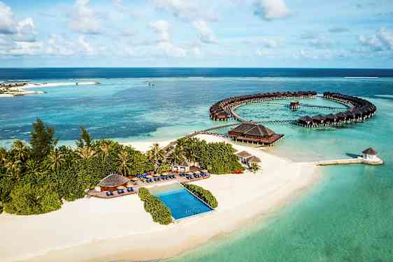 Ilmakuva trooppisesta rannikosta hiekkarannalla, merellä ja veden yläpuolisilla bungaloweilla. (Tekoälyn luoma teksti)