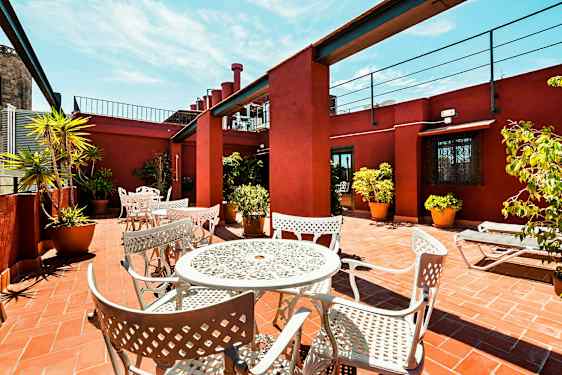 Terassi, jolla on valkoiset metallikalusteet ja ruukkukasveja tiililattialla, ympäröitynä punaisilla seinillä. (Tekoälyn luoma teksti)