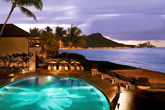 Uima-allas rannalla, ympärillä palmuja, näkymä vuoristoon ja valaistuun kaupunkiin meren rannalla. (Tekoälyn luoma teksti)