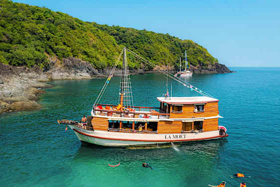 Puinen vene nimeltä 'La Moet' on kirkkaalla sinisellä vedellä lähellä metsäistä rannikkoa. (Tekoälyn luoma teksti)