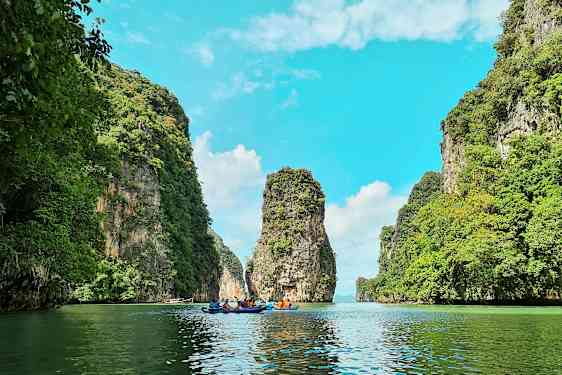 Näky rauhallisesta vesikanavasta, jota ympäröivät korkeat kallioseinät, joilla kasvaa vihreää kasvillisuutta, sekä ryhmä ihmisiä värikkäissä kajakeissa. (Tekoälyn luoma teksti)