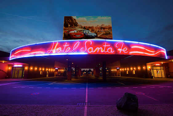 Hotel Santa Fen sisäänkäynnin yläpuolella oleva neonvalaistus, jonka yläpuolella on Disney/Pixar-autojen juliste. (Tekoälyn luoma teksti)