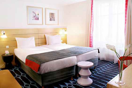 Hotellihuone, jossa on kaksi erillistä vuodetta, koristeellinen sängynpääty ja ikkuna valon sisäänpääsyllä. (Tekoälyn luoma teksti)