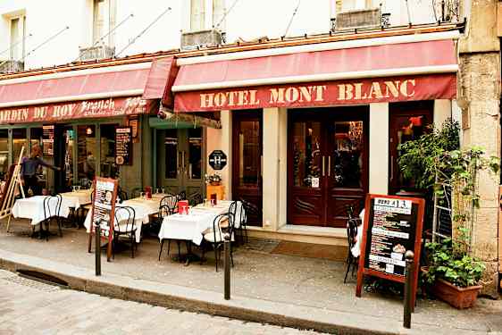 Hotellirakennuksen ulkopuolella, jossa ravintolan pöytiä ja tuoleja on asetettu jalkakäytävälle. (Tekoälyn luoma teksti)