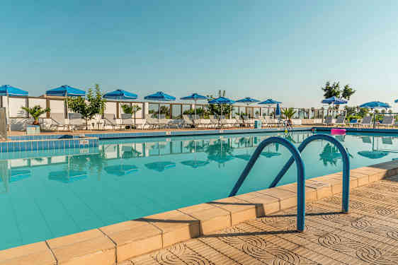 Ulkoilma uima-allas, jonka ympärillä sinisiä aurinkovarjoja ja aurinkotuoleja. (Tekoälyn luoma teksti)