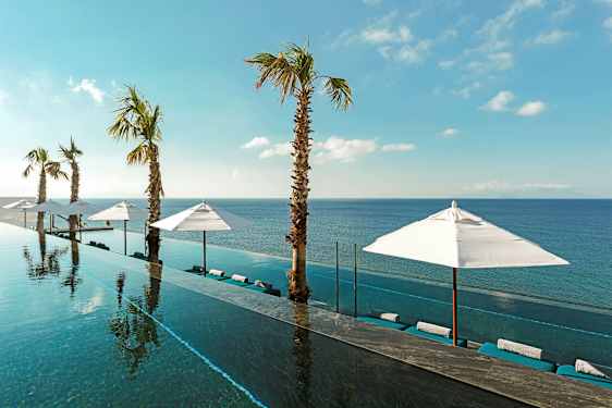 Infinity-allas, joka avautuu merelle, ympäröitynä aurinkovarjoilla ja palmupuilla kirkkaan sinisen taivaan alla. (Tekoälyn luoma teksti)