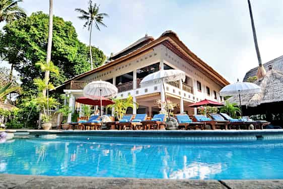 Iso huvila olkikatolla ja uima-allas edessä, ympärillä aurinkotuoleja ja varjoja. (Tekoälyn luoma teksti)