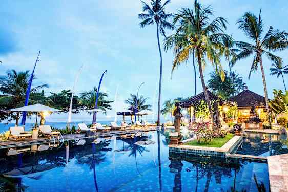 Infinity-allas, jonka ympärillä on aurinkotuoleja, aurinkovarjoja, korkeita palmuja ja avoin paviljonkialue hämärässä. (Tekoälyn luoma teksti)