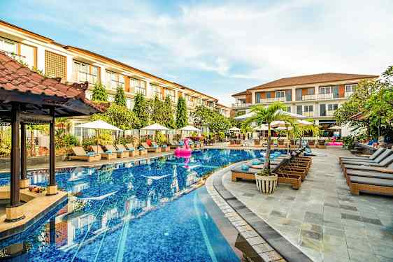 Hotellin uima-allas, jonka ympärillä on aurinkotuoleja ja aurinkovarjoja sekä taustalla rakennuksia. (Tekoälyn luoma teksti)