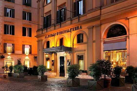 Hotelli, jonka sisäänkäyntiä koristaa kaarihallikäytävä ja jossa on valoja illalla. (Tekoälyn luoma teksti)